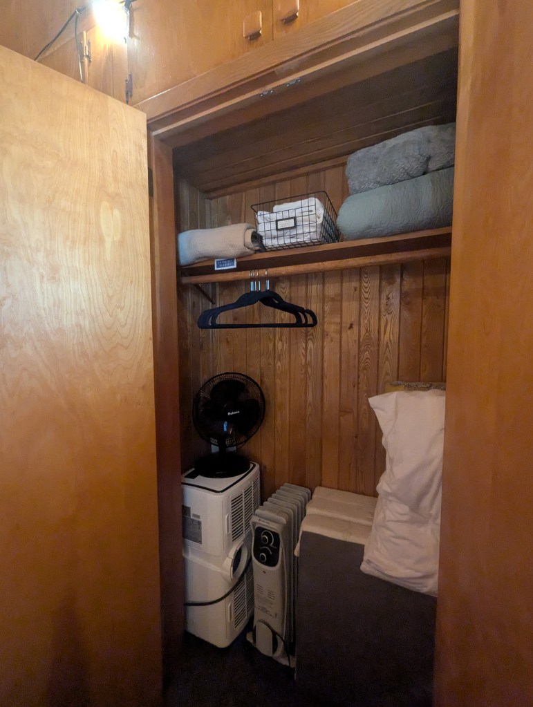 closet with extra linens, space heater, fan, hangers, and spare folding mattress