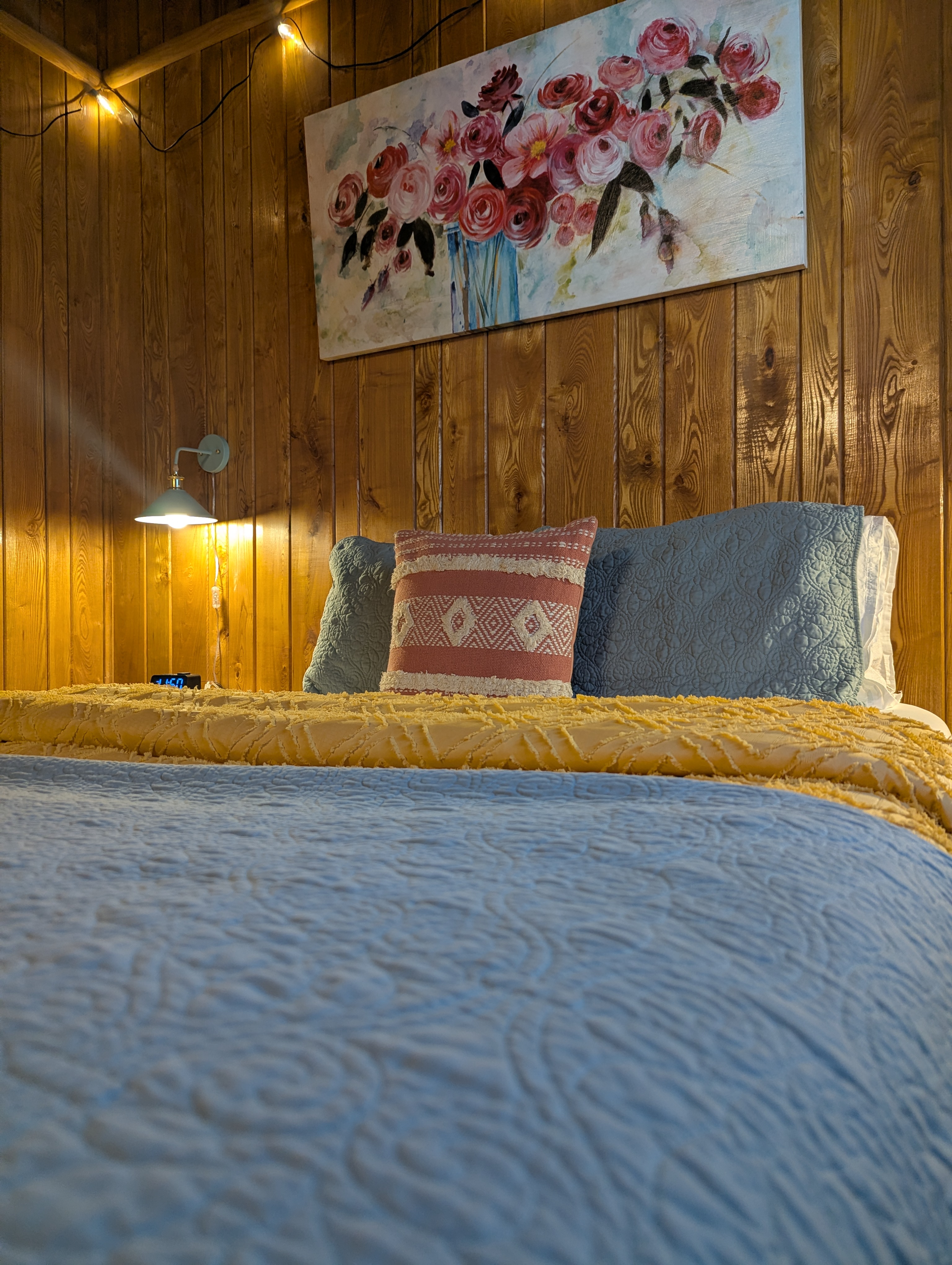 Head board wall of bed that is made with bright color bedding and flower painting hanging on the wall