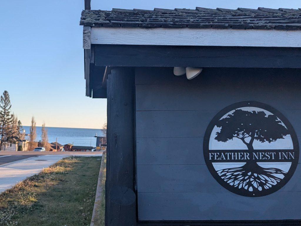 Front sign for Feather Nest Inn with lake superior in the background