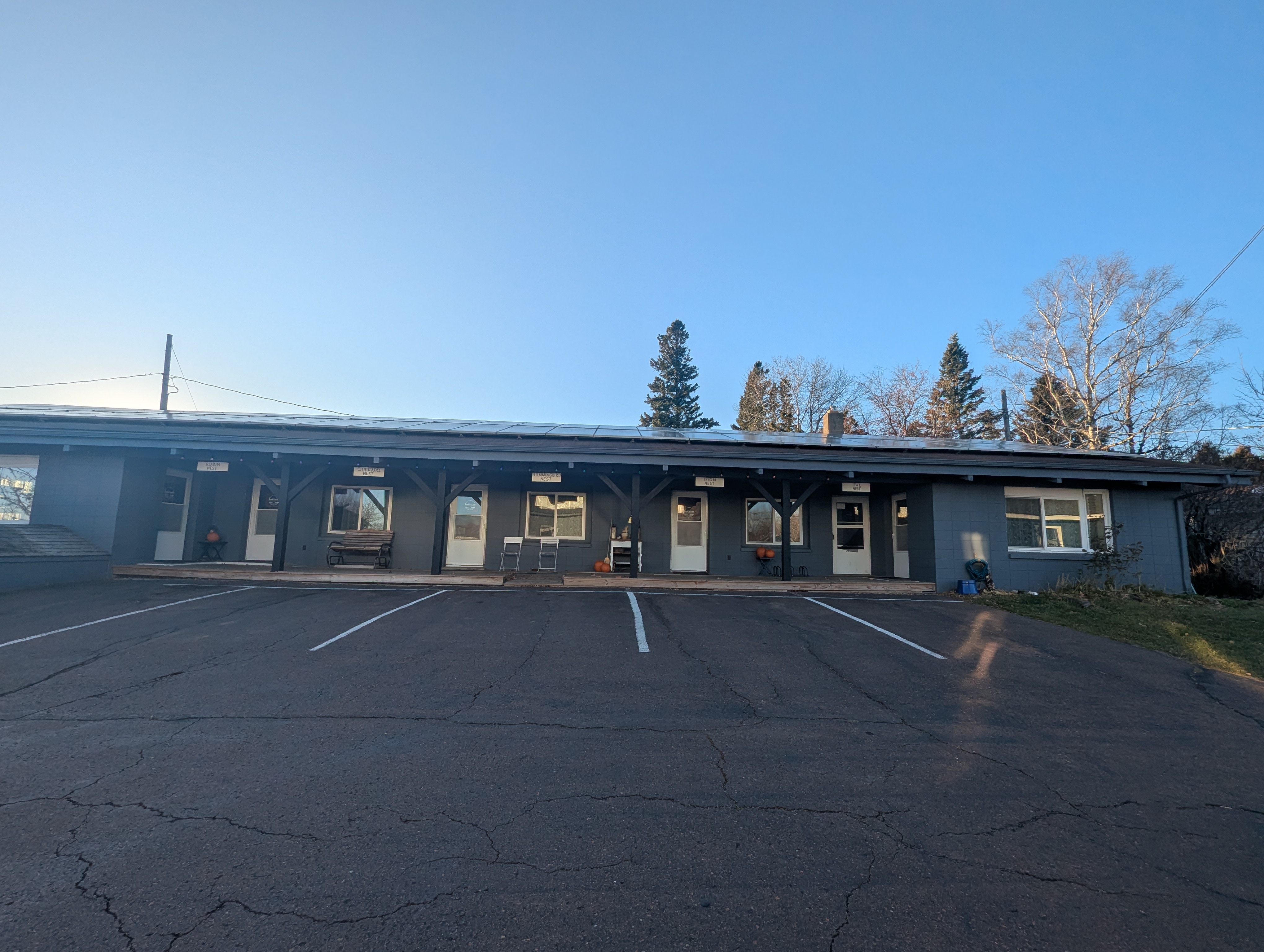 Front of Inn building shows guest door access, covered deck, roof solar panels, and parking spaces.