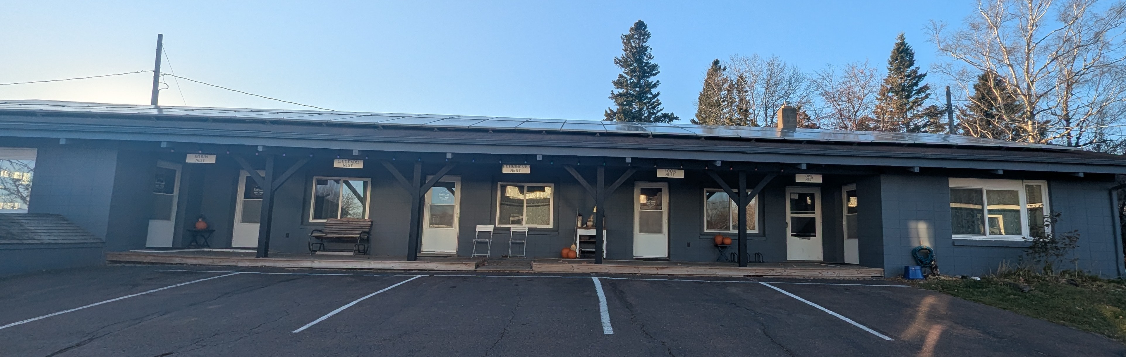 Front of Inn building shows guest door access, covered deck, roof solar panels, and parking spaces.
